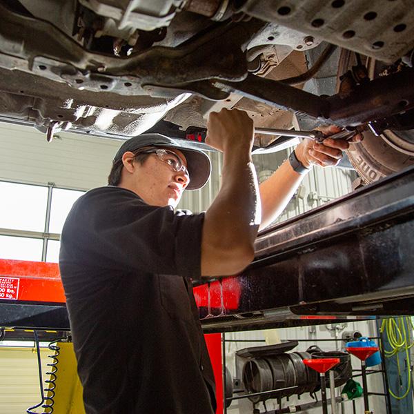 A young man working on a car on a lift.