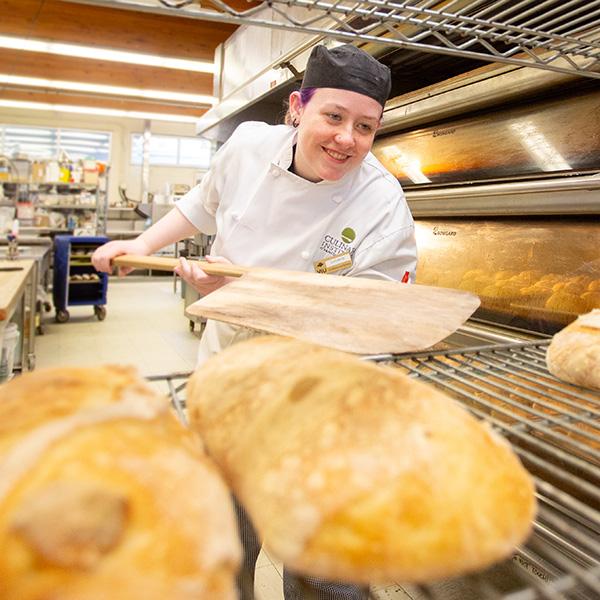 A baking student putting bread out to cool.