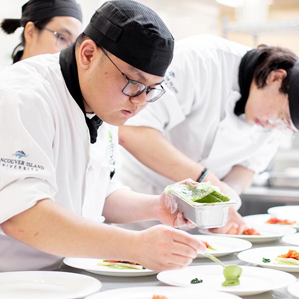 Man in chef's whites plating food. 