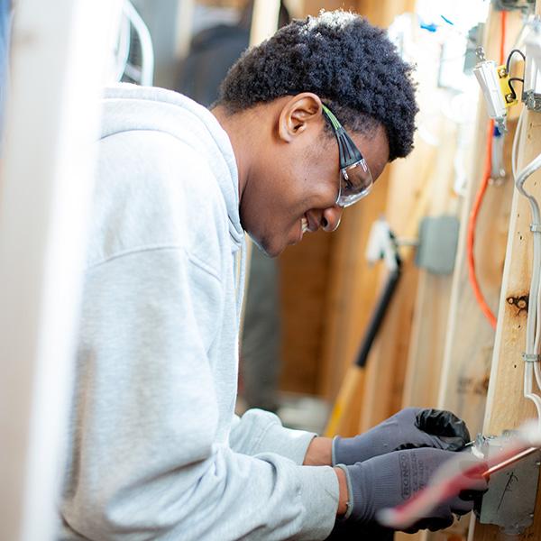 A young man works on electrical in a wall. 