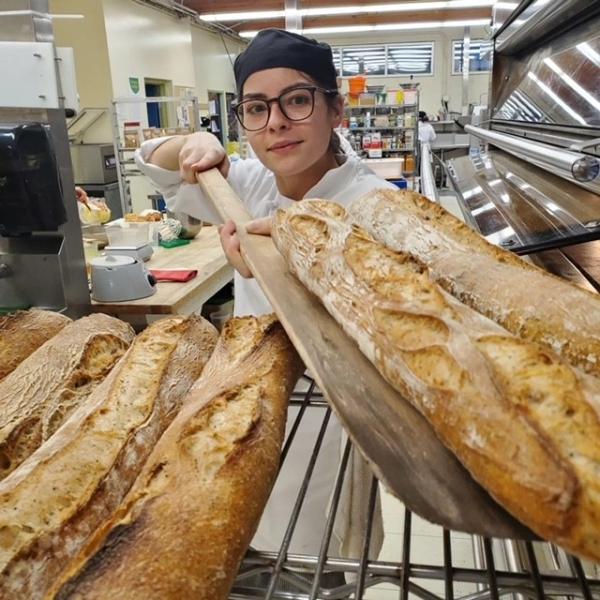 A baking student taking bread out of an oven